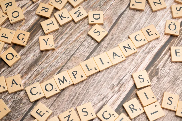 Wooden letter tiles forming the word 'COMPLIANCE' on a rustic wooden background. Build an AI content operations delivery model that survives audit