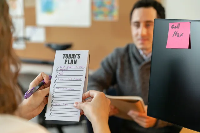 Two colleagues organizing tasks with a plan and sticky notes during a team meeting. Run an AI content operations quality checklist before you scale