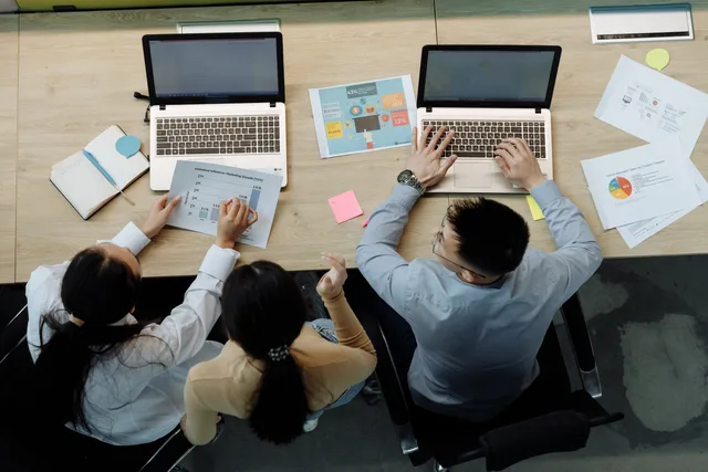 Three colleagues working on laptops and documents at a desk, collaborating on business projects. Which AI content operations software selection criteria matter most?