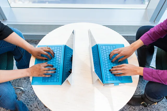 Two people working on blue laptops at a round table, focusing on teamwork and technology. What AI content operations tool implementation means for buying teams