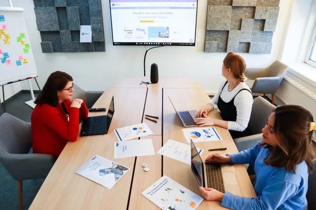 Three women collaborating in a modern office with laptops and presentation materials. Budget for the AI content operations outlook before you renew licences