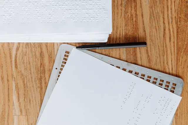 A detailed braille document on a wooden table with a metal slate and stylus, highlighting tactile writing for the visually impaired. How to audit AI content operations for UK accessibility law